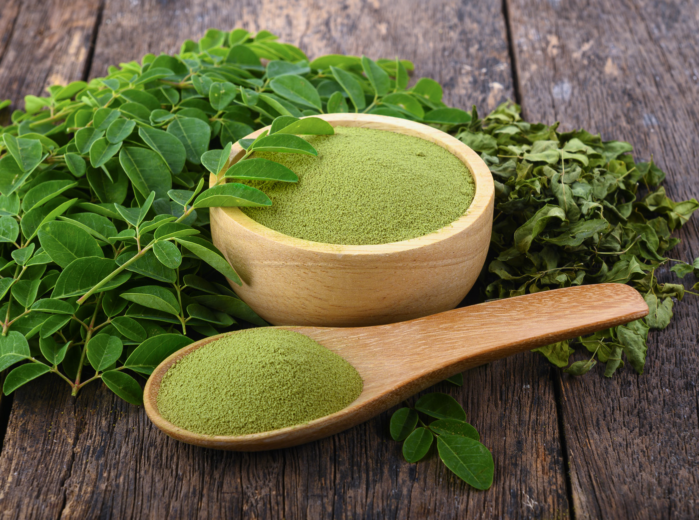 Moringa powder in wooden bowl with fresh Moringa and dried leav