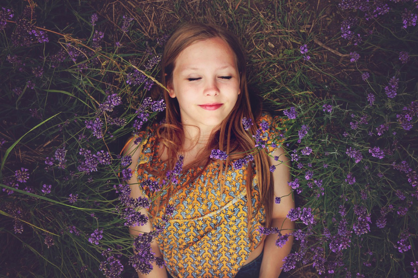 woman smiling with eyes closed taking a break in a field of purple flowers