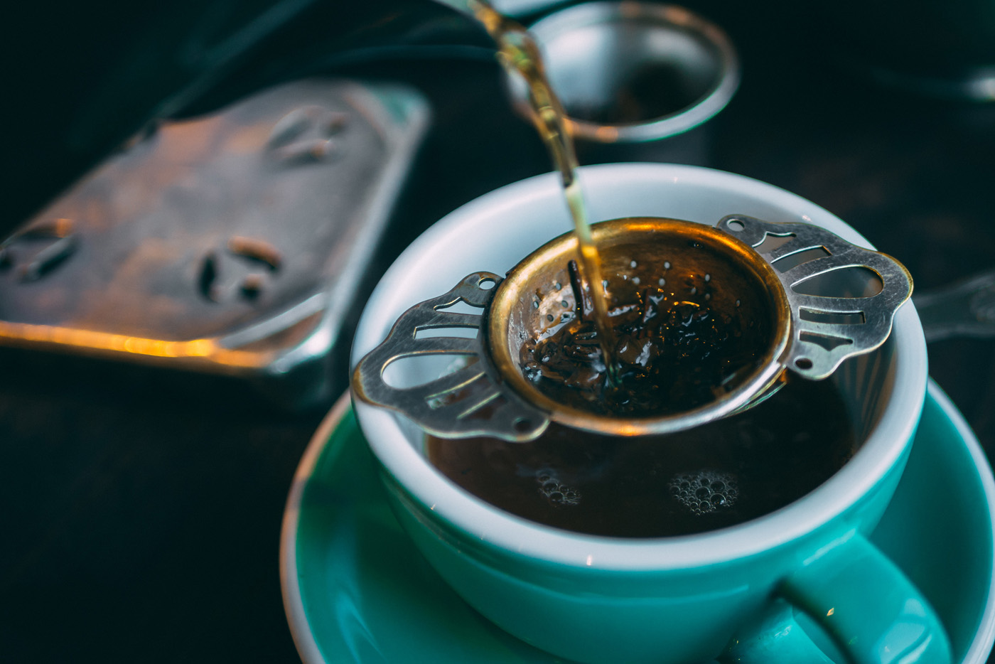 Tea pouring into strainer in blue teacup