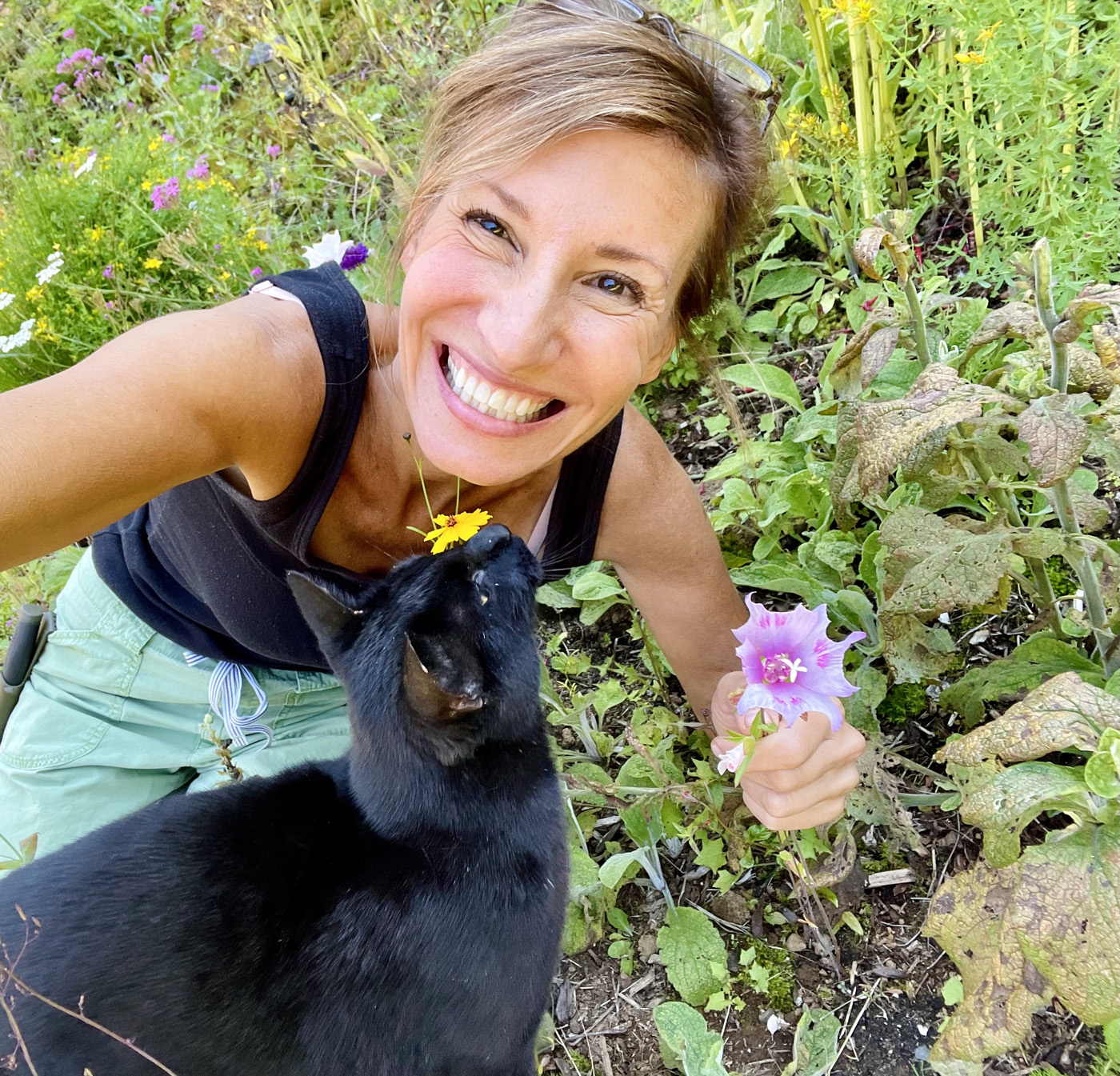 Nicole Apelian in her garden with cat Jet and a marshmallow flower