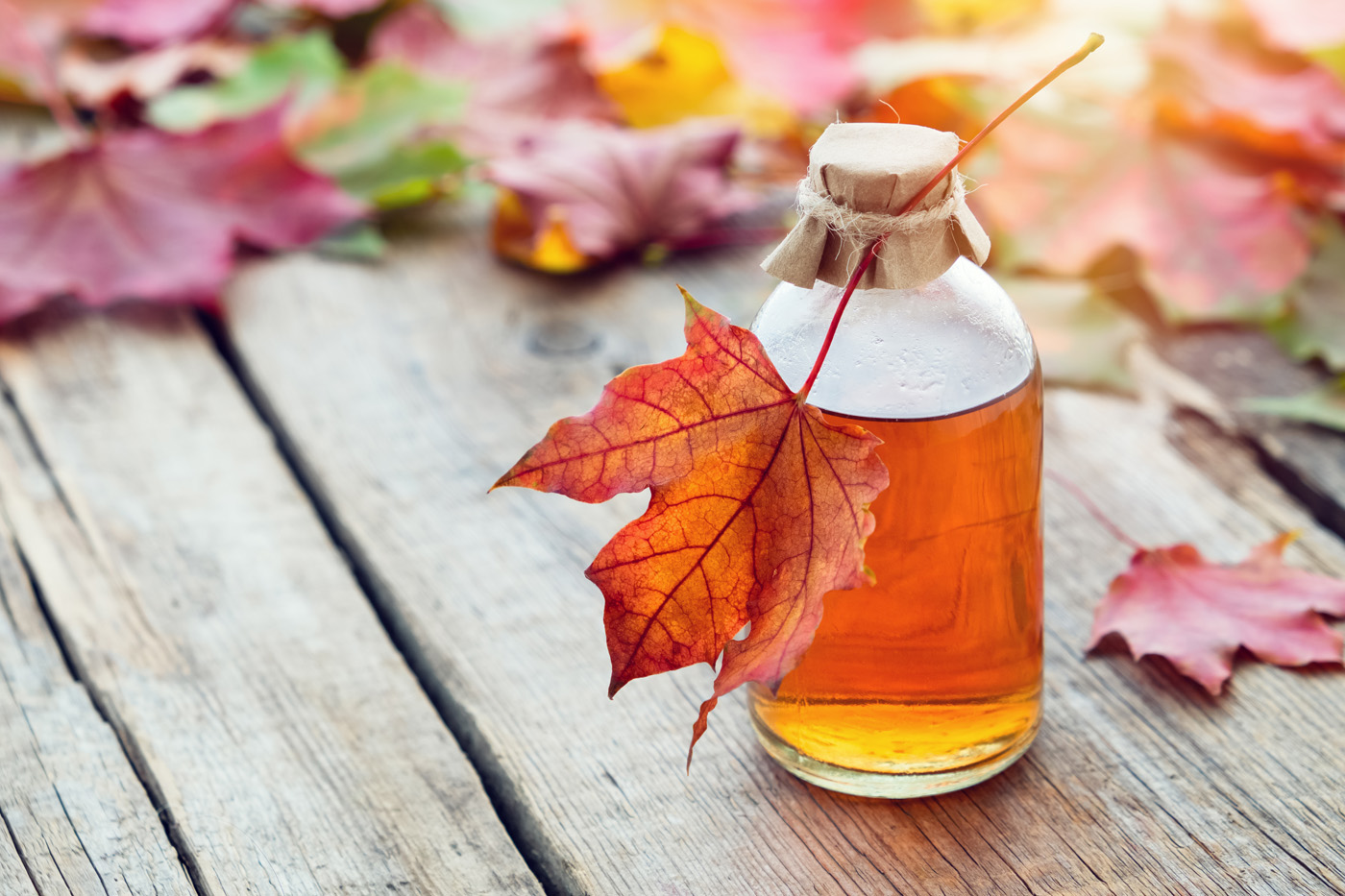 Maple syrup in bottle and fallen maple leaves.