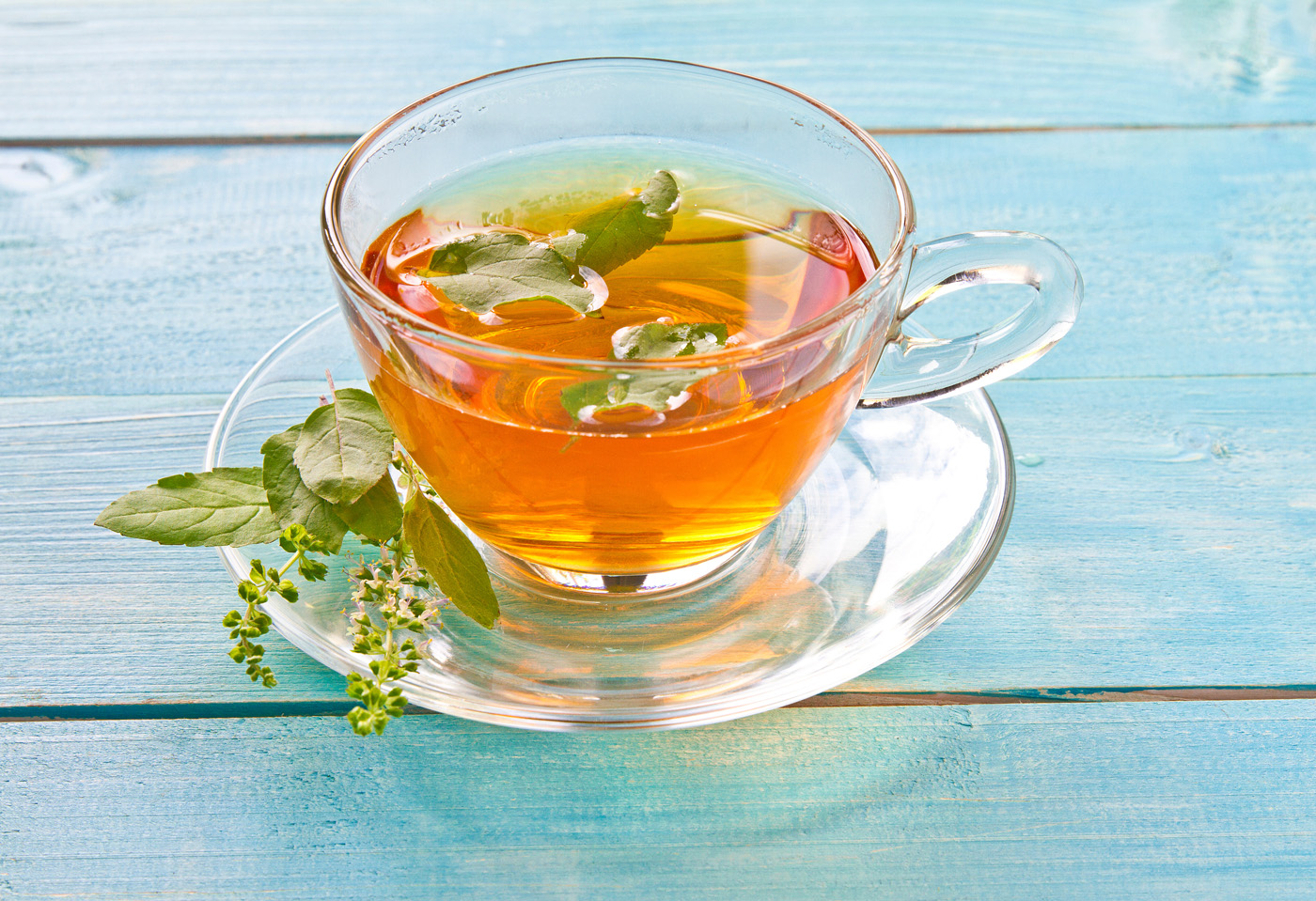 Basil tulsi tea served in a glass cup with tulsi or holi basil leaves.