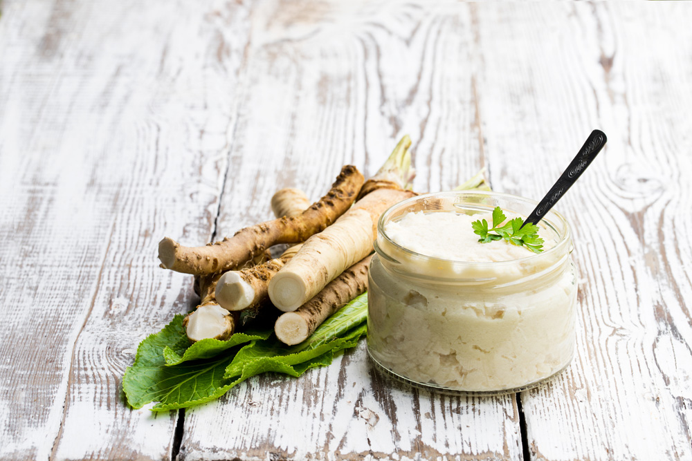 Spicy horseradish sauce in small glass jar on wooden table