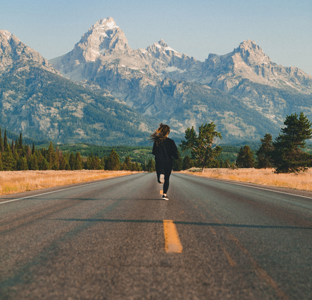 woman running down road toward mountains