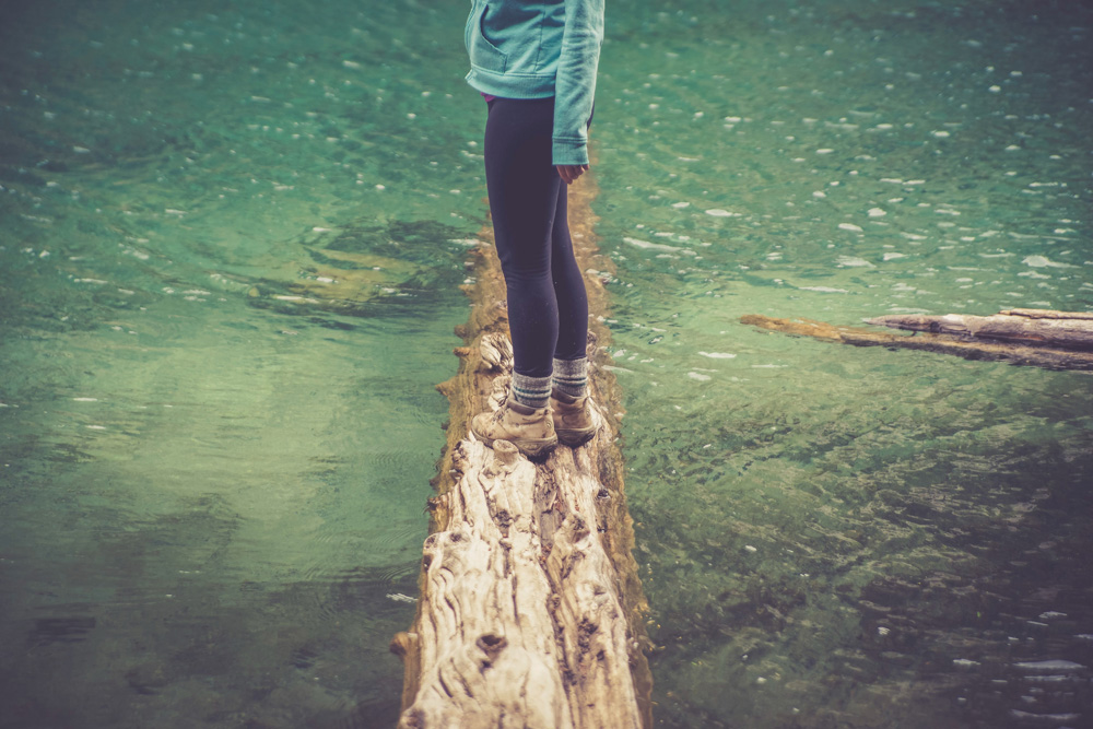 woman standing on log in river