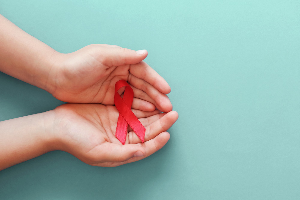 Hands holding red ribbon on blue background, hiv awareness