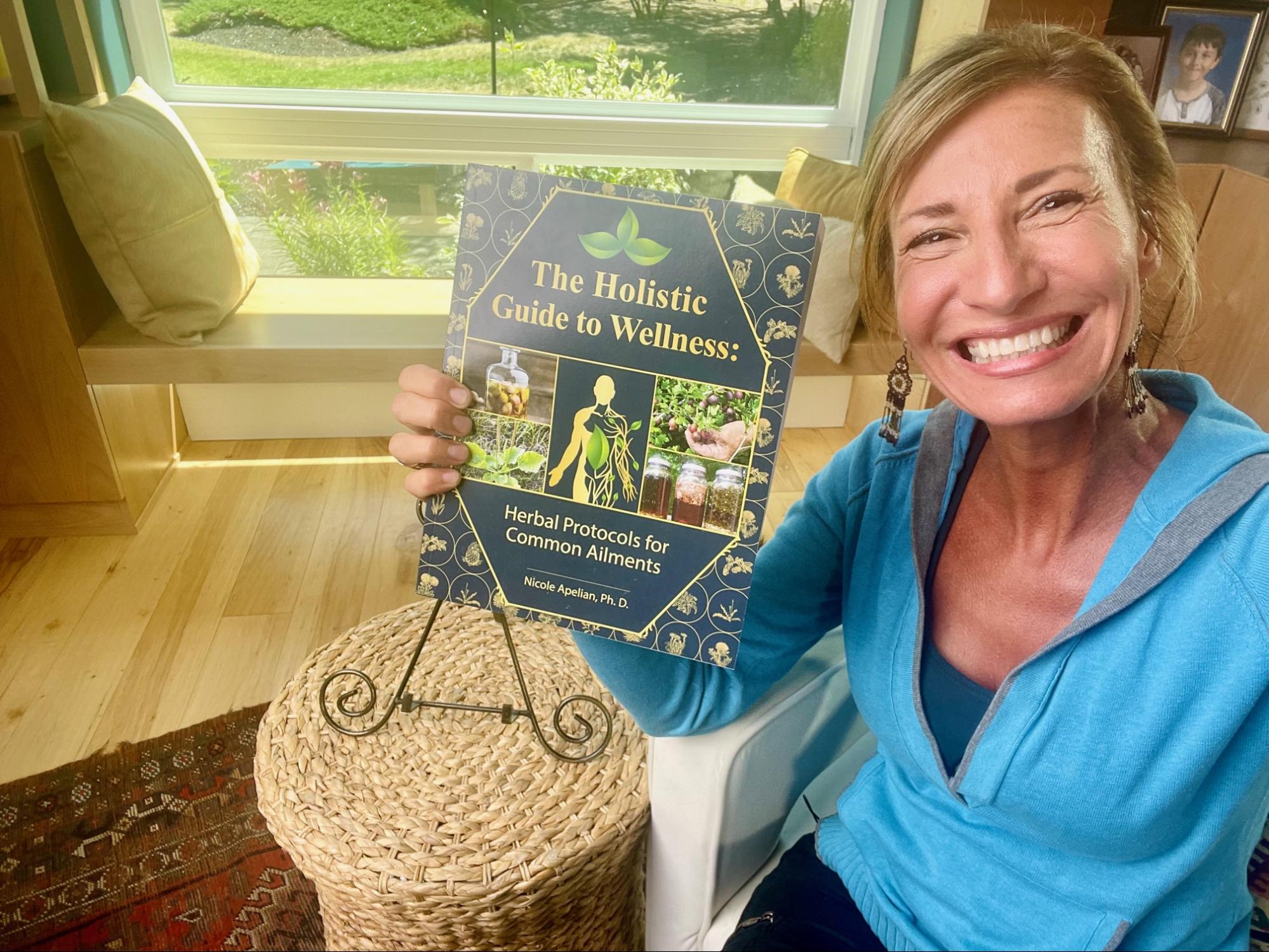 Nicole Apelian holding her Holistic Guide to Wellness book