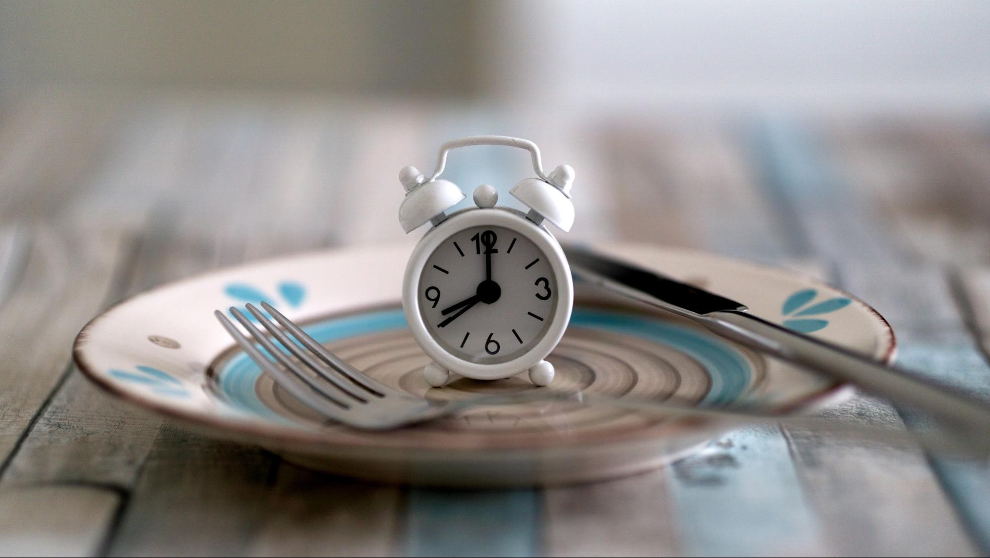 analog alarm clock on plate with silverware