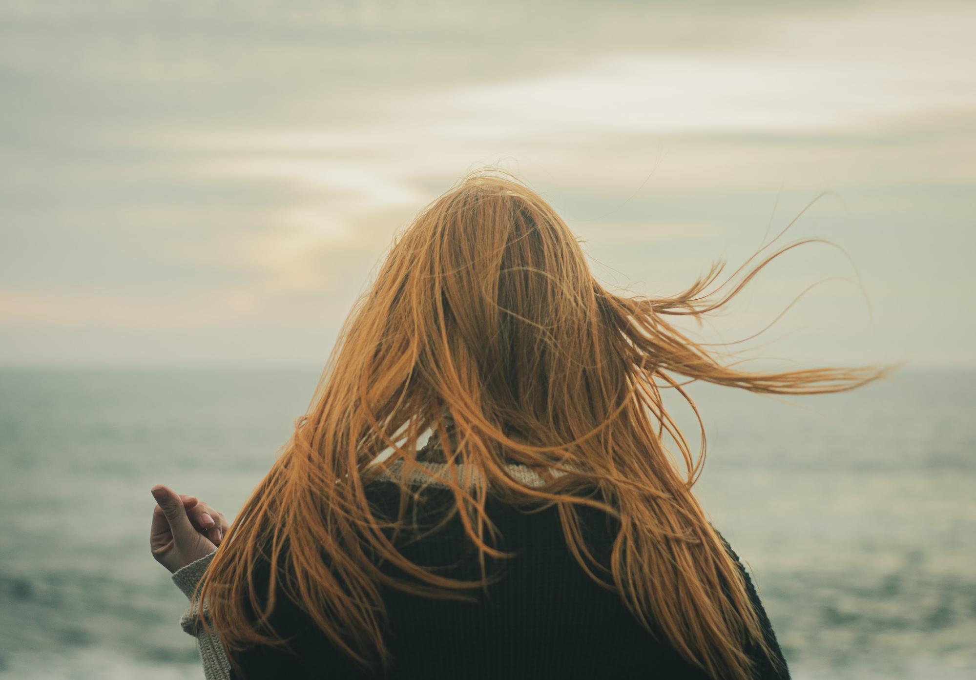 woman with red hair facing the ocean