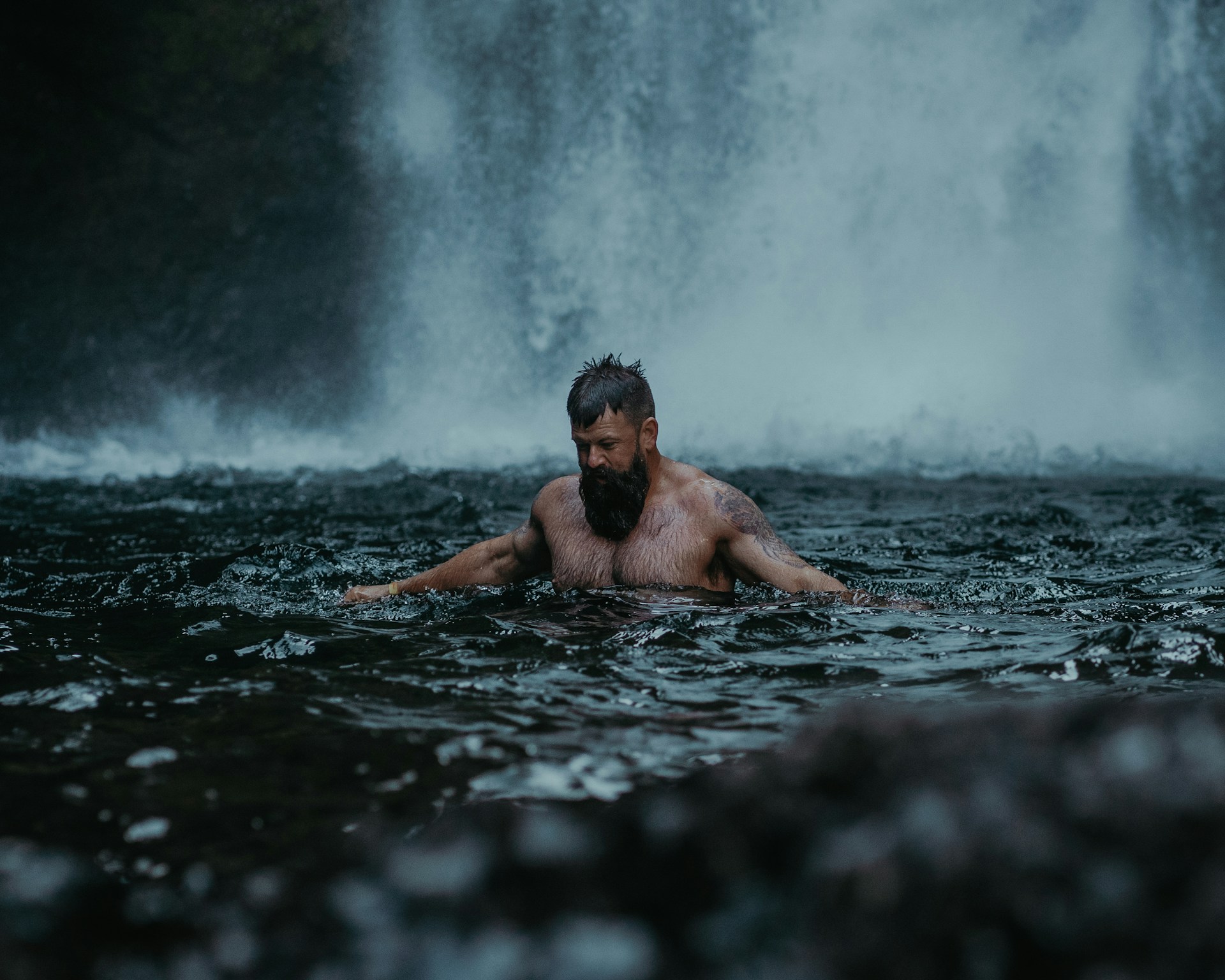 man bathing in waterfall pool