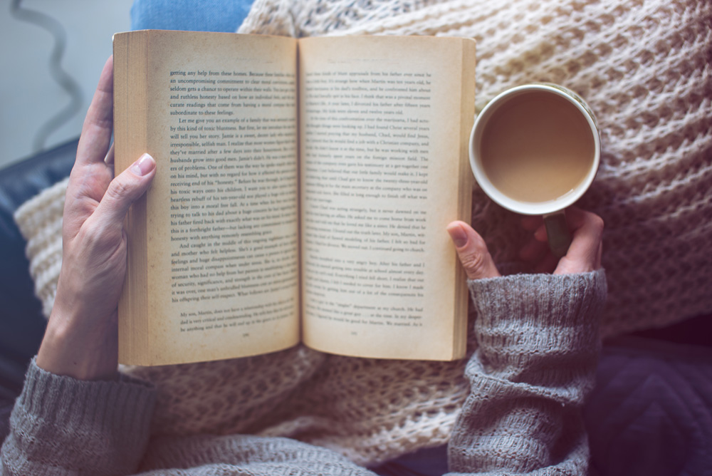 a woman is reading a book and holding coffee a woman is reading a book and holding coffee